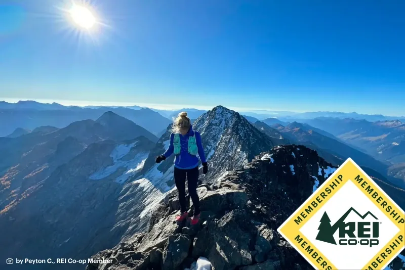 A hiker on a mountain ridge with rei membership logo.
