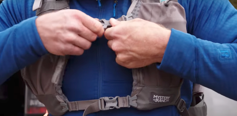 Close-up of a person adjusting sternum straps on a Mystery Ranch Bridger 55 backpack harness system.