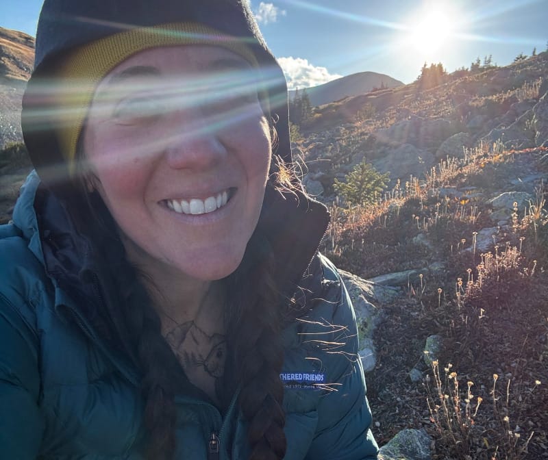 Ibex Mammoth Full-Zip Hoodie worn under a Feathered Friends down jacket with sun flare in alpine terrain.