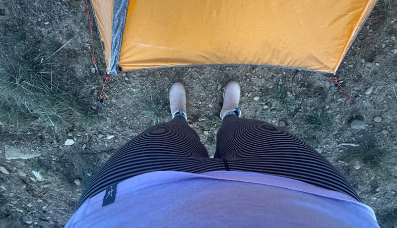 View from above showing Ibex Woolies Pro Tech base layers and tent setup on rocky ground, demonstrating outdoor use and fit.