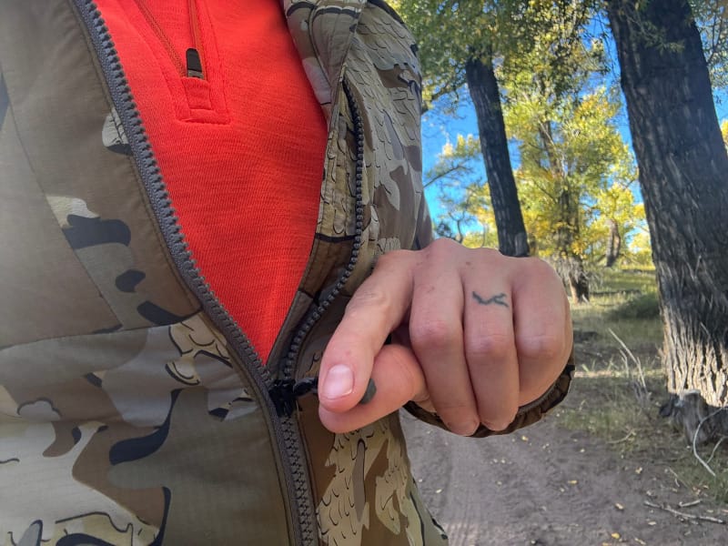 Close-up of KUIU Kenai Hooded Jacket partially unzipped over an orange base layer during a fall hike.