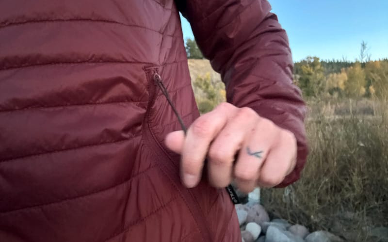 Close-up of hand zipping side pocket on PAKA Mayu Ultralight Jacket in red.