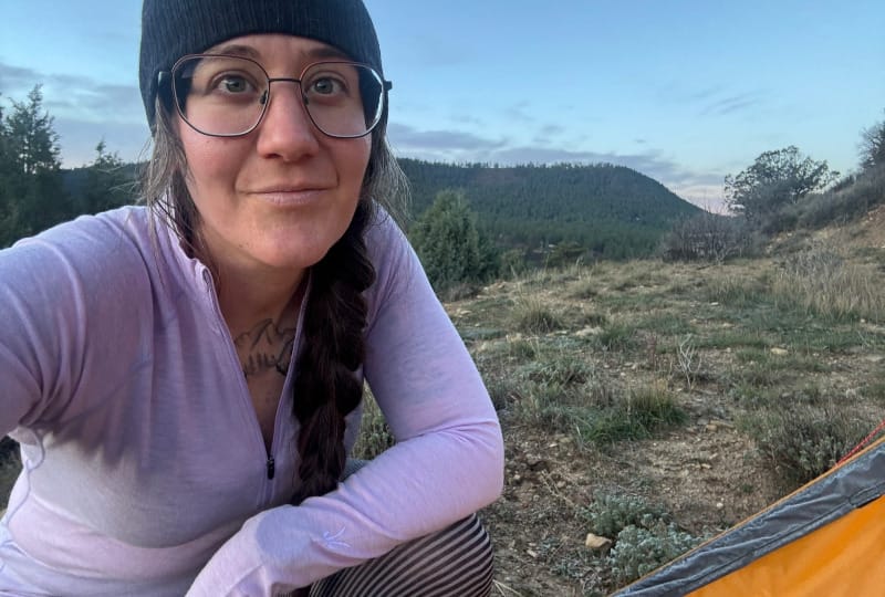 Hiker wearing the Ibex Woolies Pro Tech Half Zip merino base layer while camping in the mountains, showing relaxed outdoor setting and layering comfort.