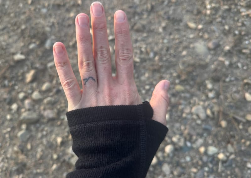 Close-up of hand wearing black PAKA Thermal Crew with thumbhole cuff, showing flatlock stitching and smooth alpaca fabric texture.