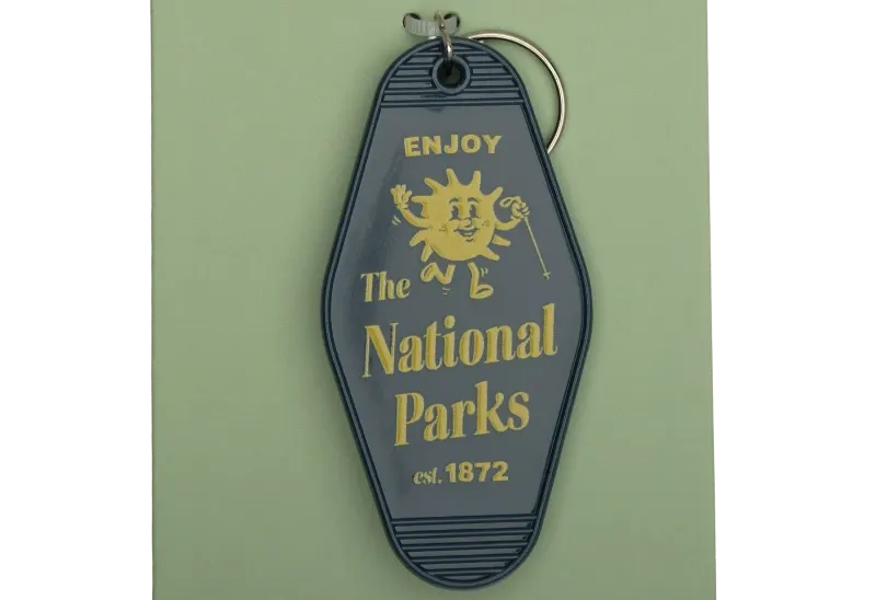 “Retro motel-style keychain reading ‘Enjoy The National Parks est. 1872’ in gold lettering.”