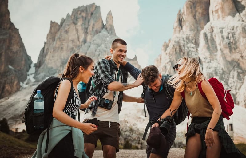 Group of happy hikers laughing together in front of dramatic mountain peaks, wearing backpacks and outdoor clothing.