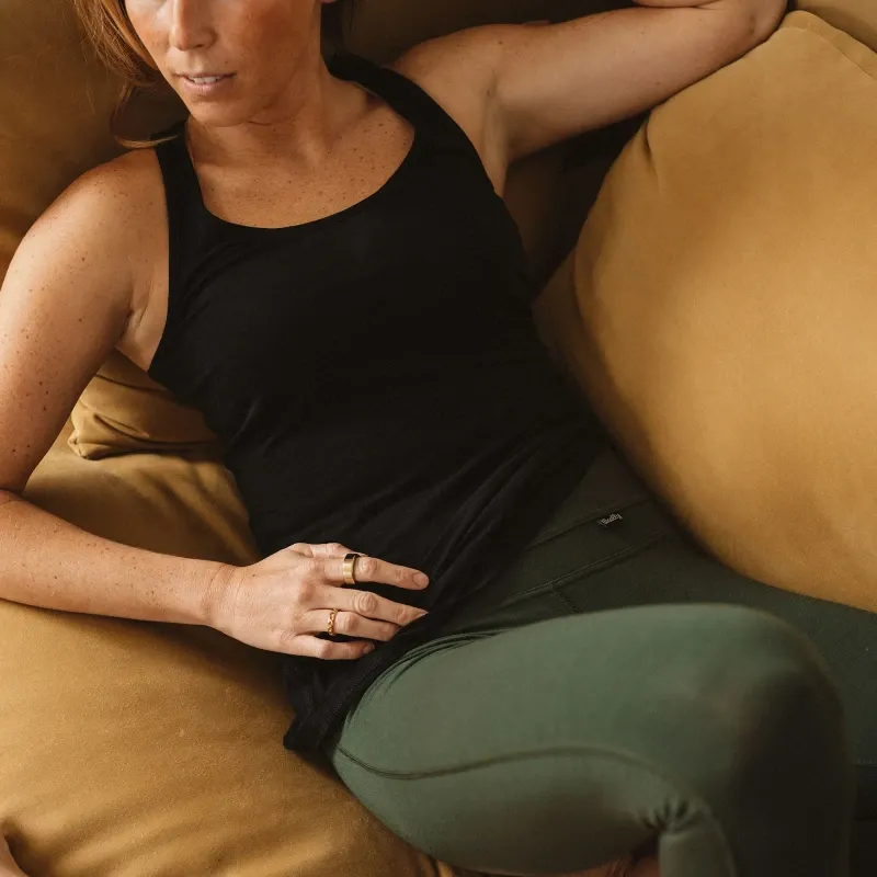 Woman relaxing on a couch wearing Woolly Clothing merino tank top and green leggings.
