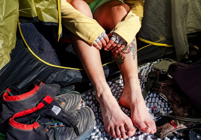 Hiker resting inside a tent with dusty hiking shoes and gaiters beside a compact first-aid kit. Wearing sun gloves
