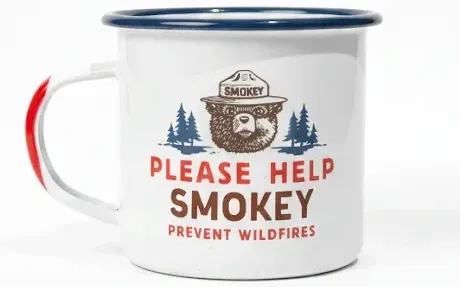 White enamel camp mug with a blue rim featuring a vintage Smokey Bear graphic and the text “Please Help Smokey Prevent Wildfires.”