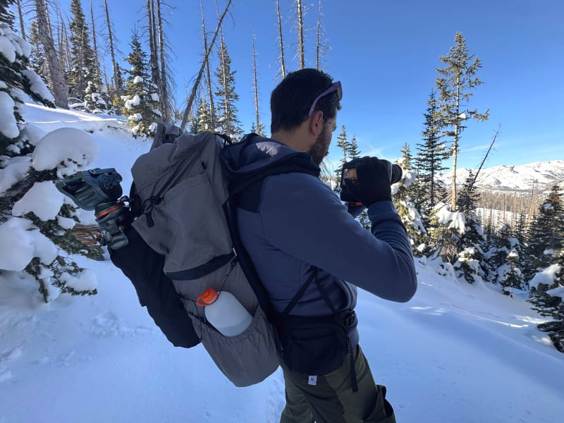 Backpacker using the Outdoor Vitals Shadowlight Carbon 60 backpack while photographing in snowy alpine terrain, showcasing pack fit and gear accessibility.