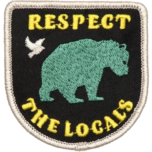 “Embroidered patch with a green bear silhouette, yellow lettering reading ‘Respect the Locals,’ and a small bird illustration.”