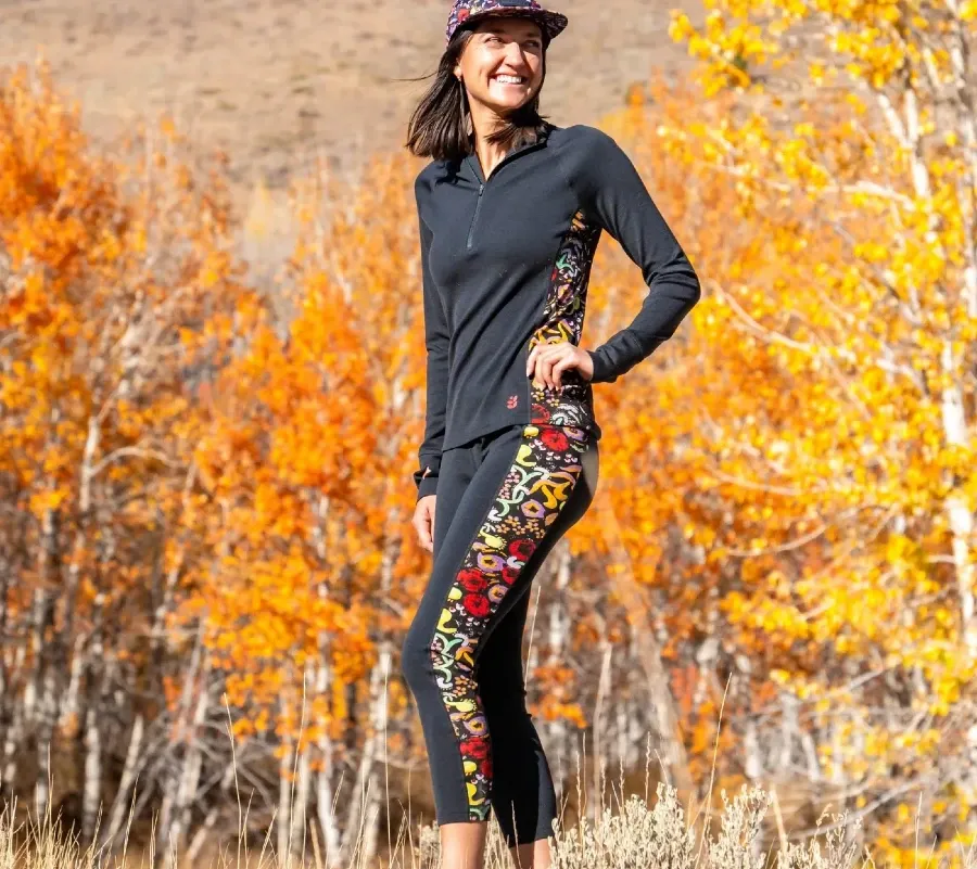 Woman standing outdoors in the full Wild Rye Bassett baselayer set with patterned side panels and fall trees in the background.