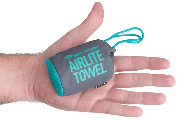 Compact Sea to Summit AirLite towel in its gray and teal carrying case held in a hand for size reference.