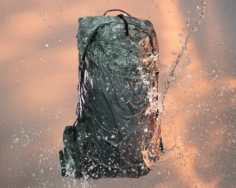 Ultralight Gossamer Gear Alchemy backpack suspended in midair as water splashes around it, highlighting the pack’s weather resistance.