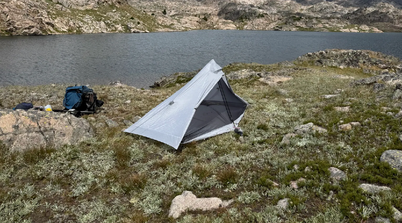 Ultralight solo backpacking tent pitched near an alpine lake in rocky mountain terrain, showing a lightweight trekking pole shelter setup