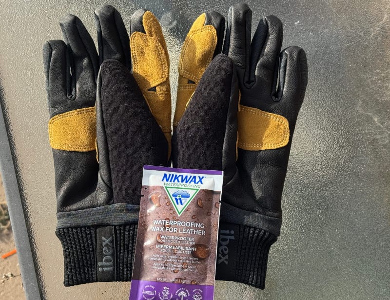 Ibex Kilometer Gloves flat lay showing merino wool construction, leather palm overlays, and leather care wax