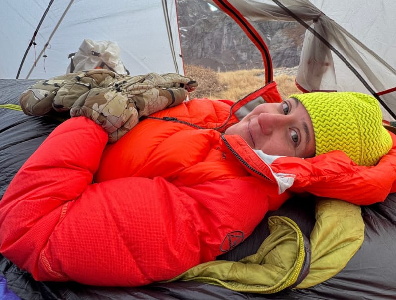 Person resting inside a backpacking tent while wearing KUIU Super Down Pro Glomitts, showing their warmth and insulation in cold alpine conditions.