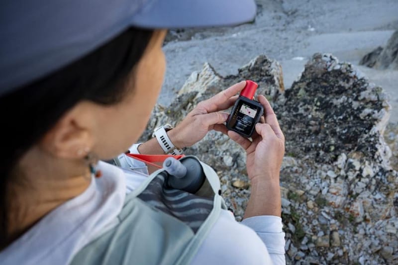 Hiker using the Garmin inReach Mini 3 Plus satellite communicator to view messages and maps while hiking in rocky backcountry terrain.