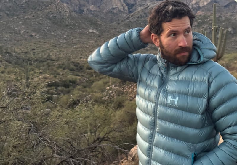 Person wearing a light blue HIMALI down jacket in a desert mountain landscape with saguaros and rocky terrain