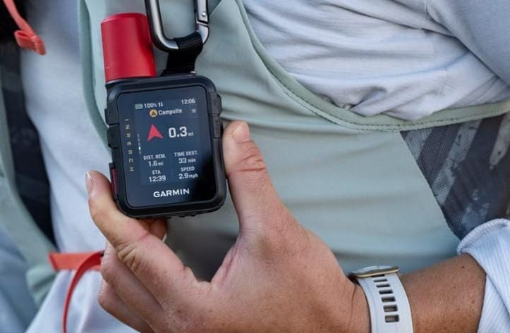 Garmin inReach Mini 3 Plus satellite communicator clipped to a backpack shoulder strap, displaying navigation and distance data during a hike.