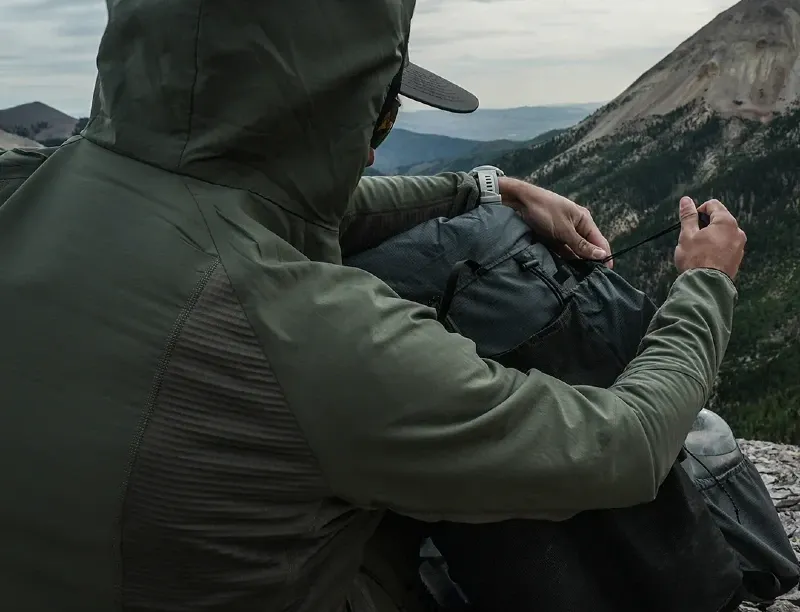 hiker wearing Outdoor Vitals Pursuit Hybrid Fleece adjusting backpack on mountain ridge during high altitude hike