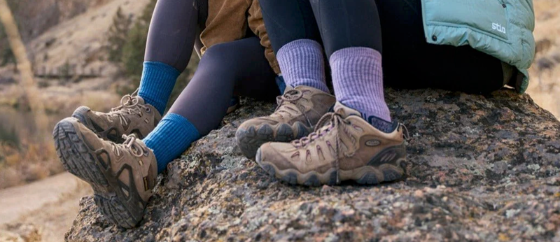 two women wear toughcutie hiking socks while on a hike. they are posed on a boulder