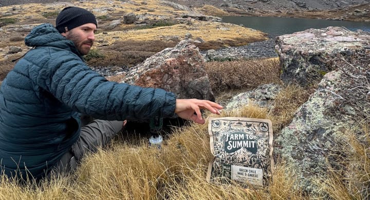 a backpacker making a farm to summit dehydrated meal with a stunning mountain in the background