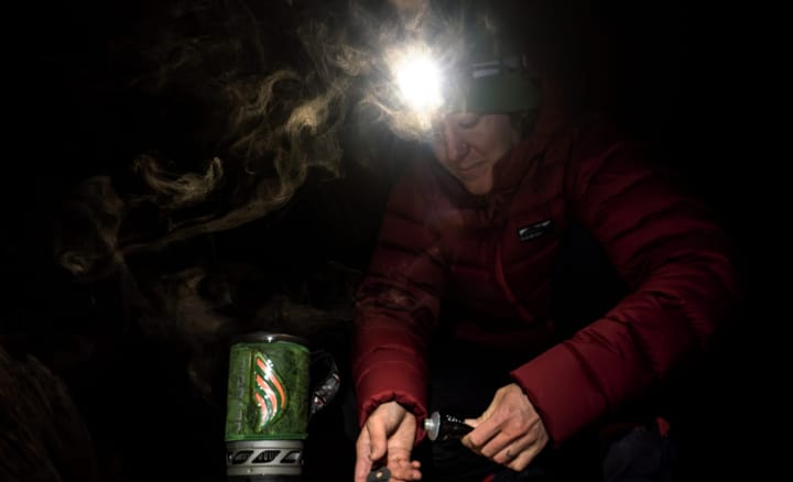  Person wearing the Black Diamond Distance 1500 headlamp while cooking with a camp stove in the dark during a cold alpine night.