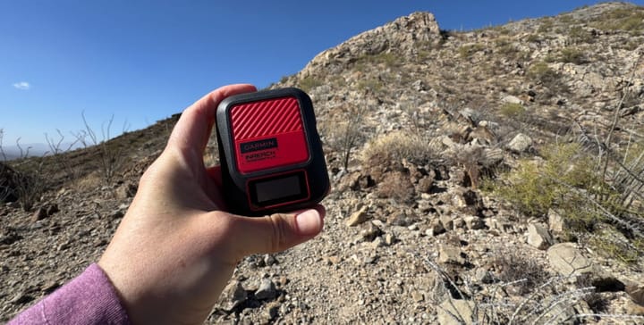  Garmin inReach Messenger Plus held in front of a rugged desert ridgeline under a clear blue sky, ready for off-grid adventure.