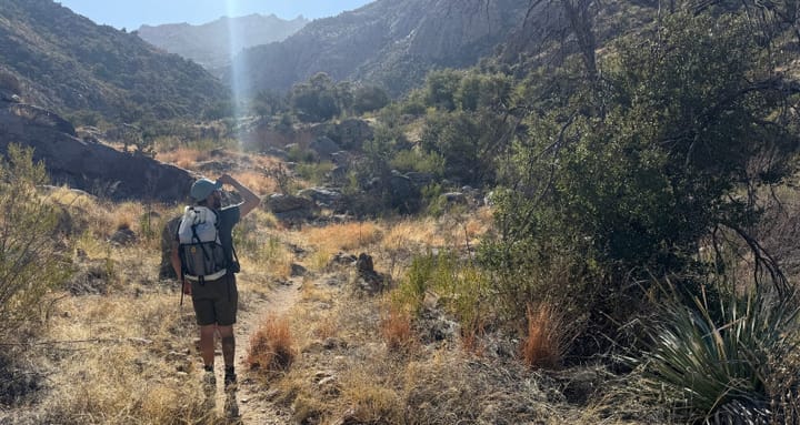  Back view of a hiker wearing the Hyperlite Mountain Gear Windrider 40 pack on a dry trail in desert mountains, walking toward distant peaks.