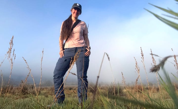 Woman wearing the Fjallraven Keb Trousers in a grassy field with fog in the background, showcasing the improved fit for Summer 2025.
