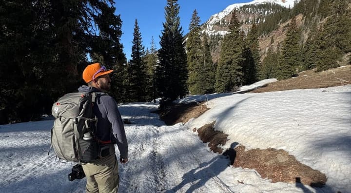 Hiker wearing the NEMO Persist 45L Backpack while trekking through snowy mountains with evergreen trees in Colorado.