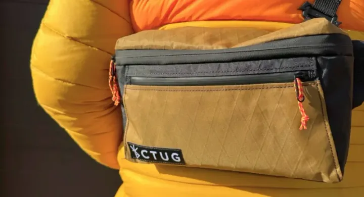Close-up of a Chicken Tramper Ultralight Gear fanny pack worn crossbody over a bright orange and yellow puffy jacket.