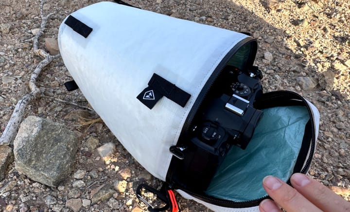 Open Hyperlite Camera Pod showing a mirrorless camera inside, sitting on desert ground