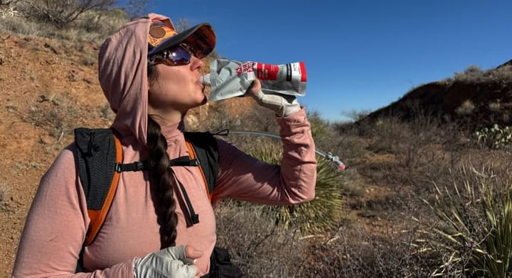 RecPak meal replacement pouches arranged with backpacking gear in a rugged mountain setting.