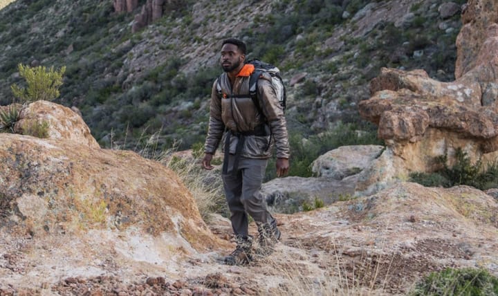  Man hiking in the desert wearing the Enlightened Equipment Torrid Jacket and carrying a large backpack.