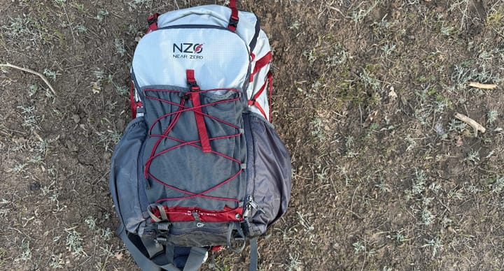  Top view of the fully packed Near Zero Dean 60 Backpack lying on dirt, showing external stretch cords and storage compartments.