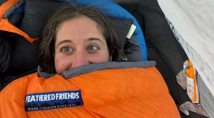 Smiling hiker bundled in a Feathered Friends Egret sleeping bag inside a tent.