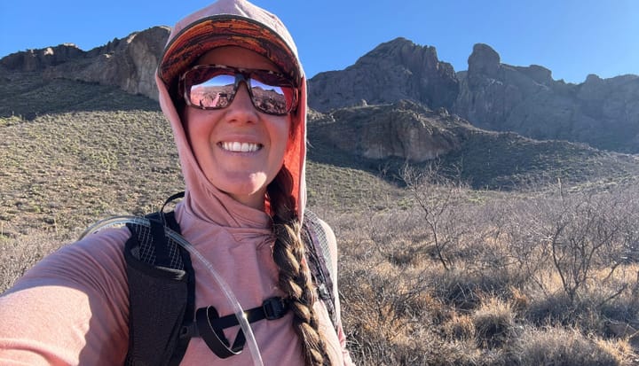  Hiker wearing the pink PAKA SOL Sun Hoodie in the Organ Mountains desert landscape with hydration pack and braided hair.