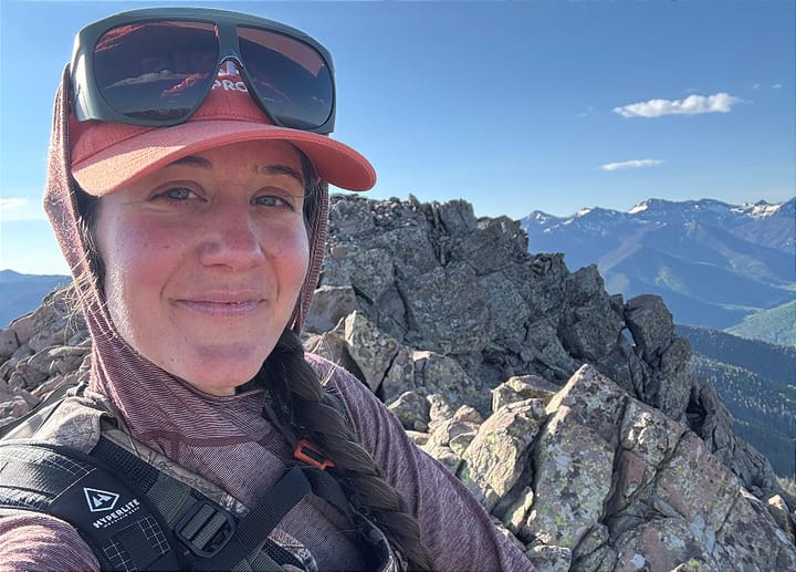 Close-up of hiker on rocky summit wearing Vuarnet Altitude 01 glacier sunglasses and camera gear.
