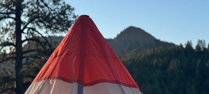  Wide-angle view of SlingFin pyramid tent pitched in a high-desert campsite with surrounding trees and hills.