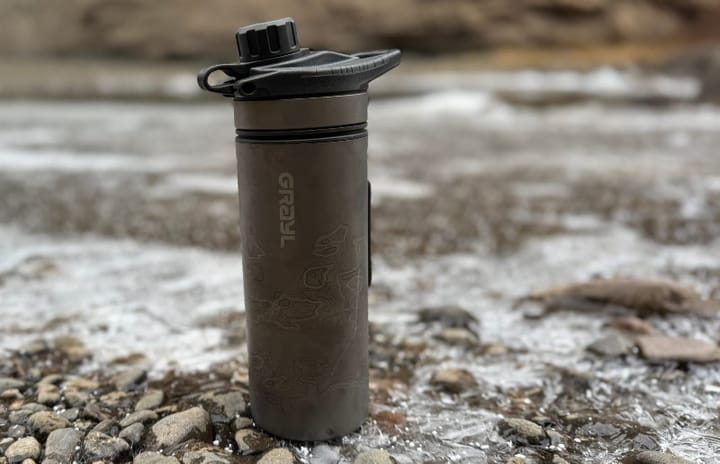 GRAYL GeoPress Ti bottle standing upright on icy river rock in a cold, rugged mountain landscape.