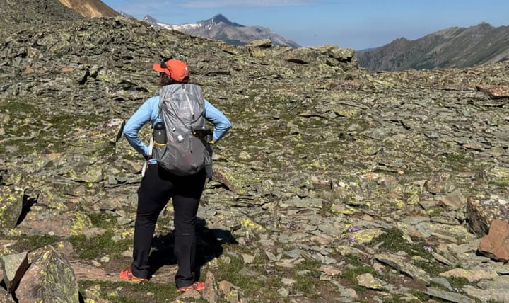  Back view of Mountain Magic 50 Pro backpack worn by hiker standing on alpine ridge trail with mountains ahead
