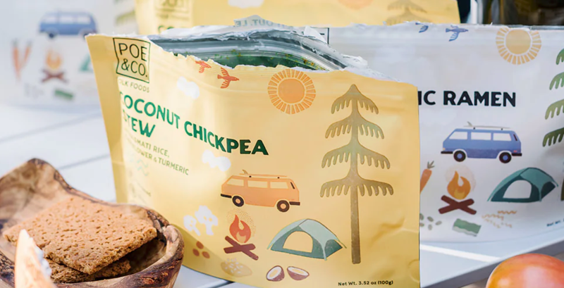  Coconut Chickpea Stew meal pouch on a white table with the Black Garlic Ramen and Quinoa Skillet in the background, next to crackers and outdoor gear.