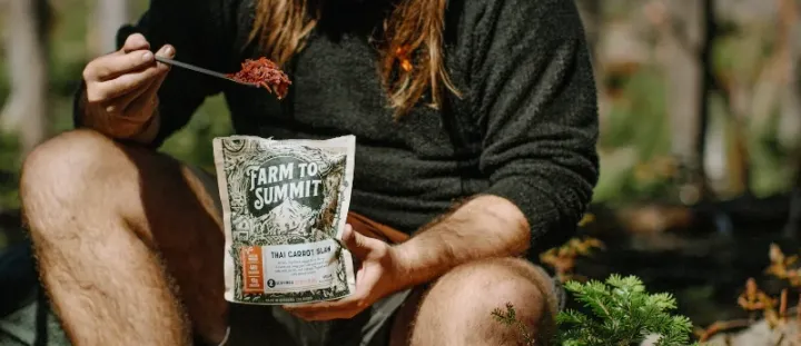 Backpacker enjoying a rehydrated Farm to Summit Thai Carrot Slaw meal while sitting in the forest.