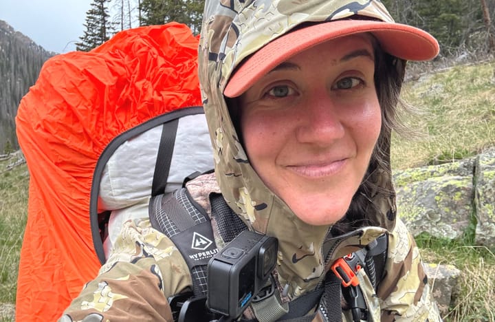 Backpacker wearing camouflage jacket with a blaze orange pack cover for added visibility on the trail.