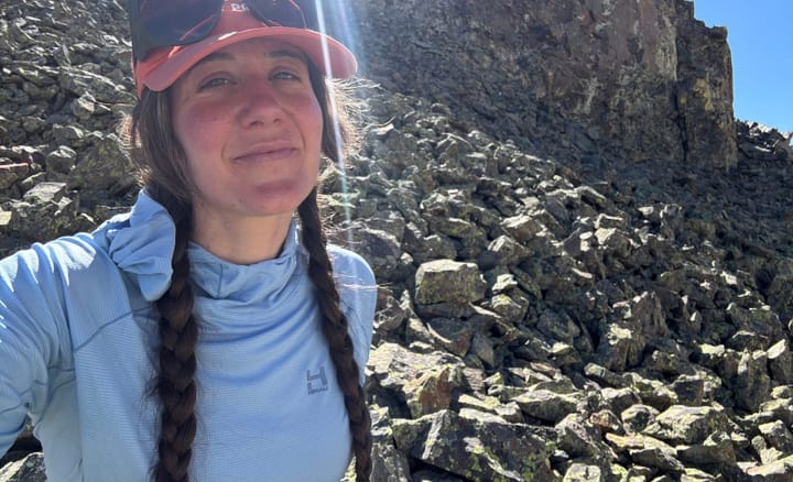 Woman wearing the HIMALI Eclipse Sun Hoodie while hiking a rocky mountain slope, showing the hoodie’s UPF protection and breathability.