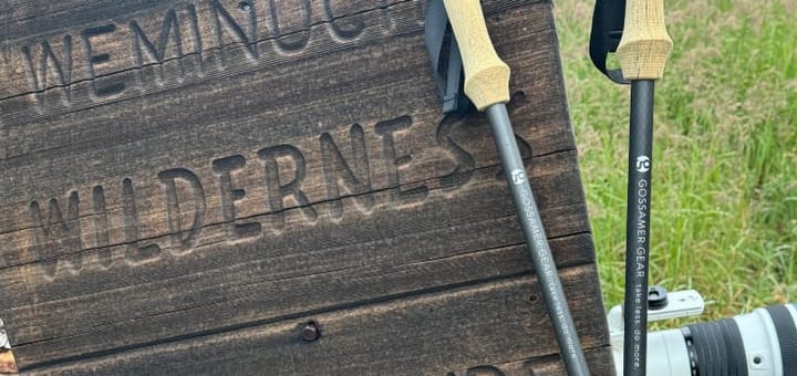 Pair of Gossamer Gear trekking poles leaning against a wooden Weminuche Wilderness sign in Colorado.