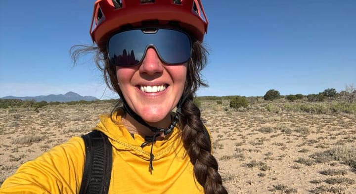  Smiling woman wearing Ombraz Refugio sunglasses and a helmet while hiking or biking in the desert.