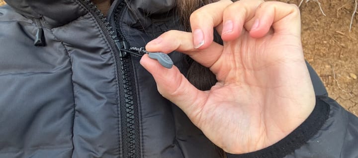 camper wearing the KUIU Elements Hooded Jacket outdoors, showing the hood and front zipper design during field testing.